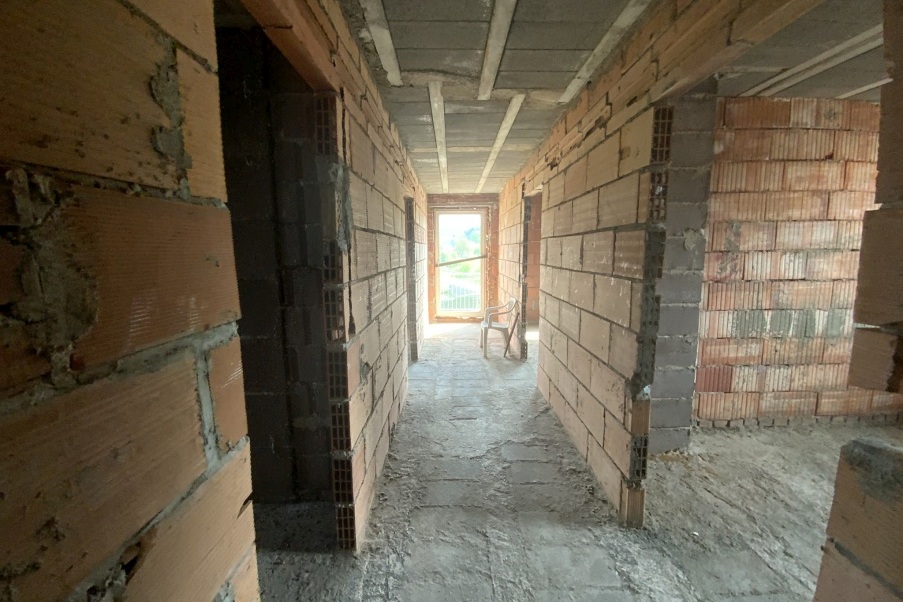 Baufortschritt: Rohbauflur mit Ziegelmauern und Fenster im Hintergrund