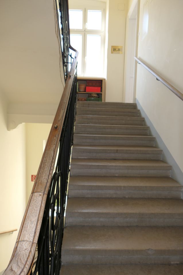 Treppe mit Holzhandlauf und schmiedeeisernem Geländer, daneben ein Regal mit Gegenständen