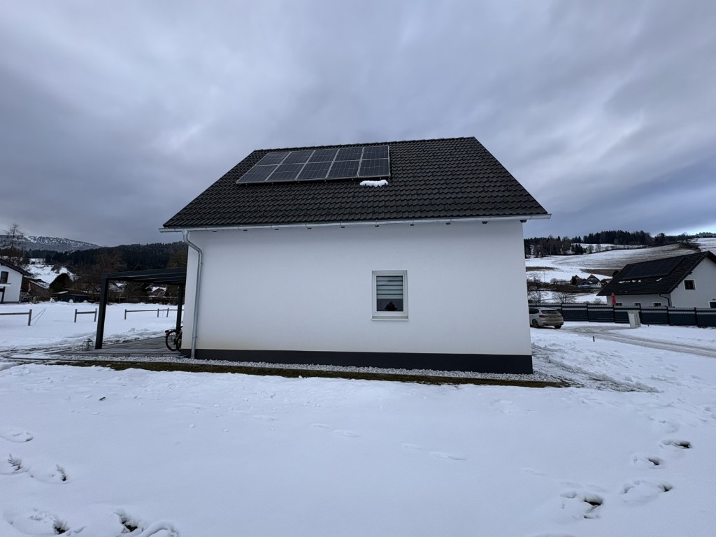 Solaranlage auf Dach eines weißen Hauses im Schnee mit Carport und Auto