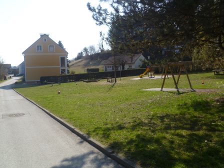 Spielplatz mit gelbem Haus und Schaukel im ländlichen Österreich