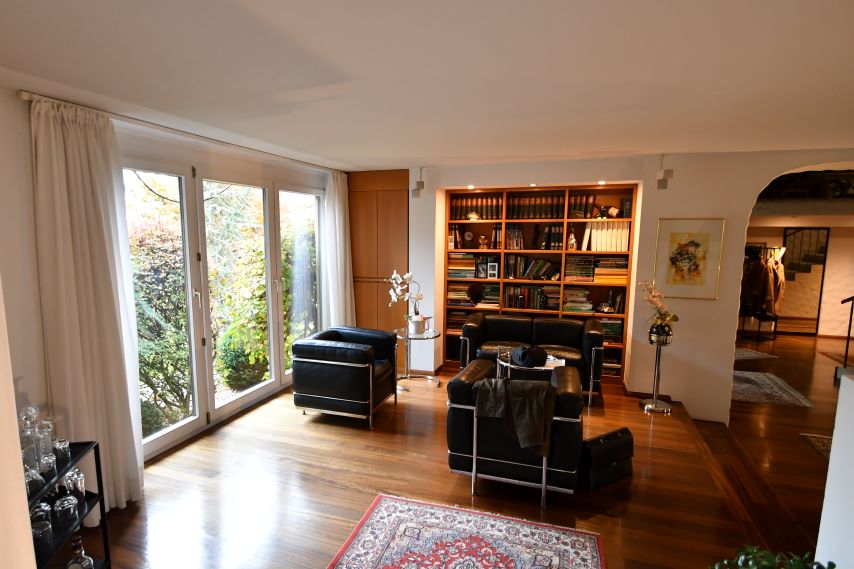 Wohnzimmer mit Ledermöbeln und Bücherregal, große Fensterfront mit Blick in den Garten