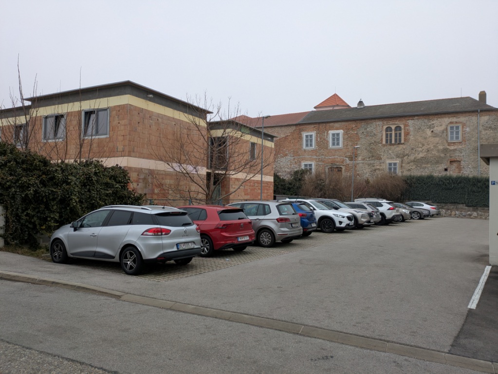 Autos auf Parkplatz vor einem Ziegelbau und einem alten Gebäude