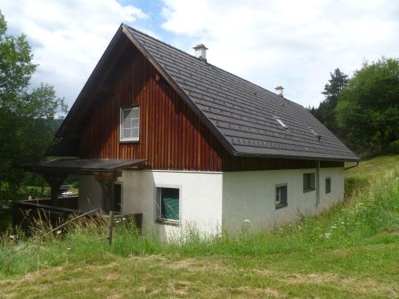 Holzhaus mit weißer Fassade und dunklem Dach in ländlicher Umgebung