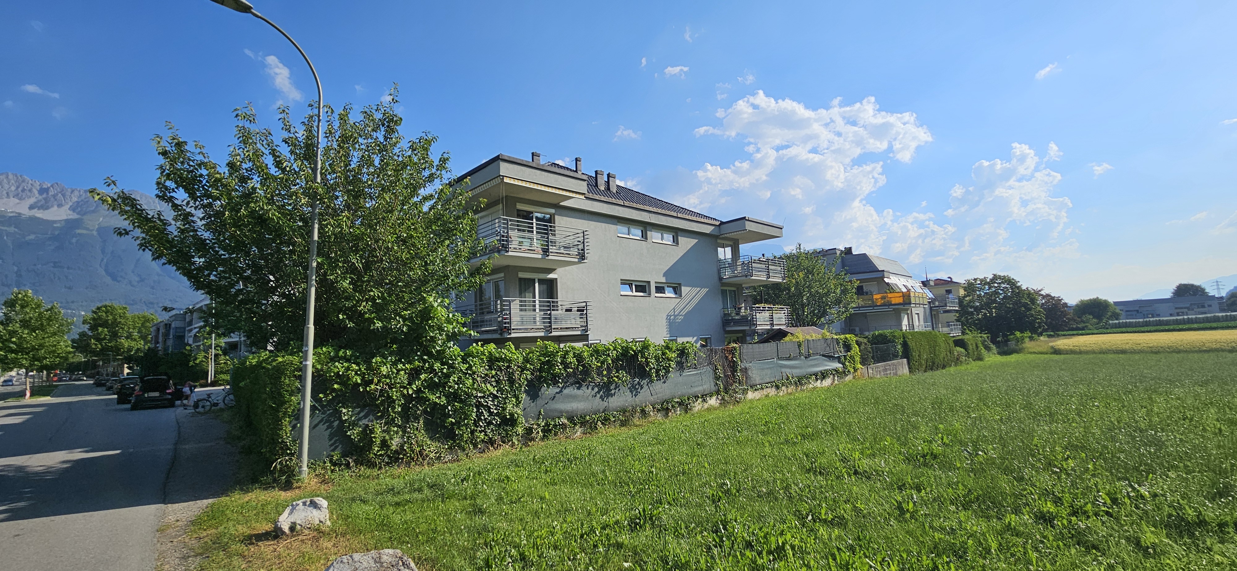Mehrfamilienhaus mit Balkonen und grüner Wiese vor Alpenpanorama