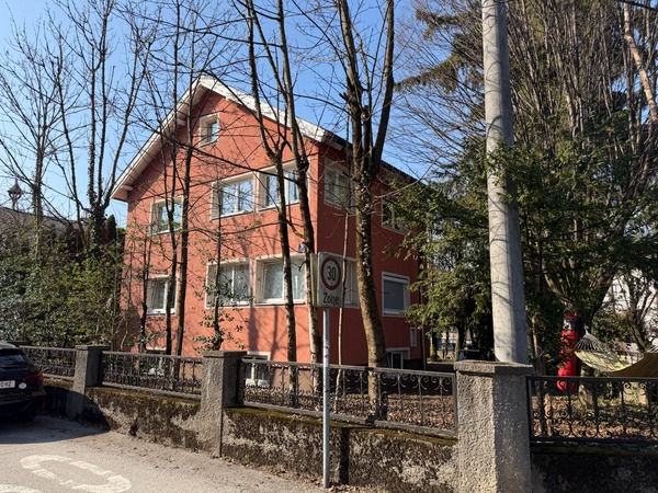 Rotes Haus mit Bäumen und einem Verkehrsschild in einer Zone 30 in Österreich