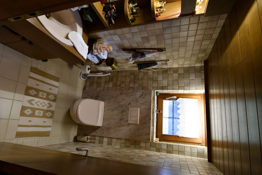 Badezimmer mit Toilette, Waschbecken und Fenster mit blauer und weißer Gardine