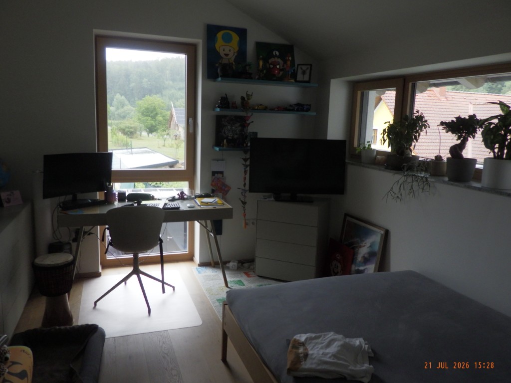 Arbeitszimmer mit Schreibtisch, zwei Fernsehern und einem Bett in einem Dachgeschoss.
