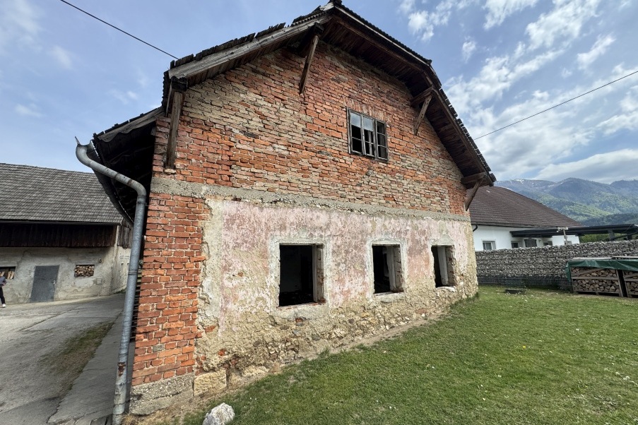Altes Ziegelhaus mit kaputtem Dach und leeren Fensterrahmen in ländlicher Umgebung.
