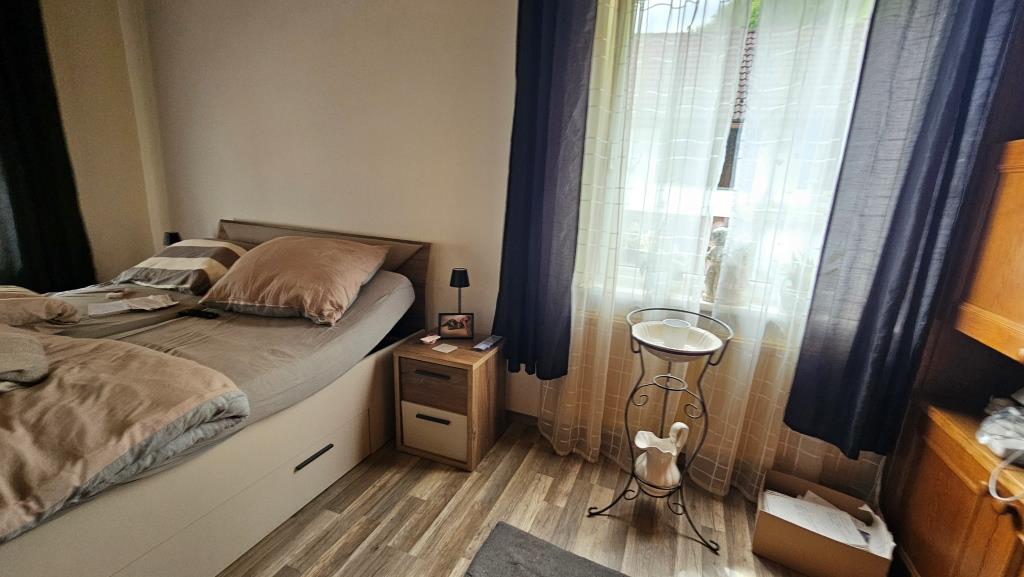 Schlafzimmer mit Doppelbett, Nachttisch, Lampe und Blumenständer mit Vase.
