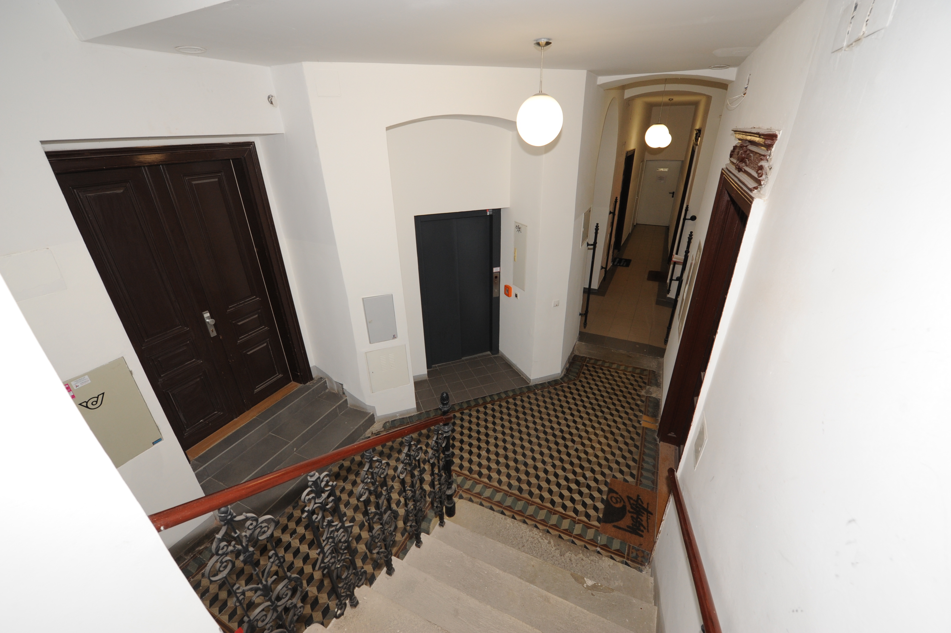 Stiegenhaus mit dunklen Türen, ornamentalem Geländer und Mosaikboden