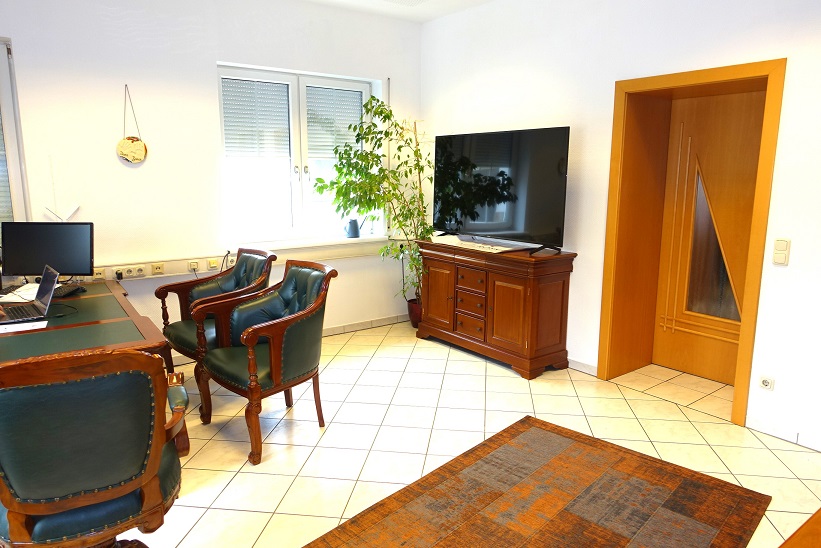 Büro mit Schreibtisch, Ledersesseln, Fernseher und Holztür
