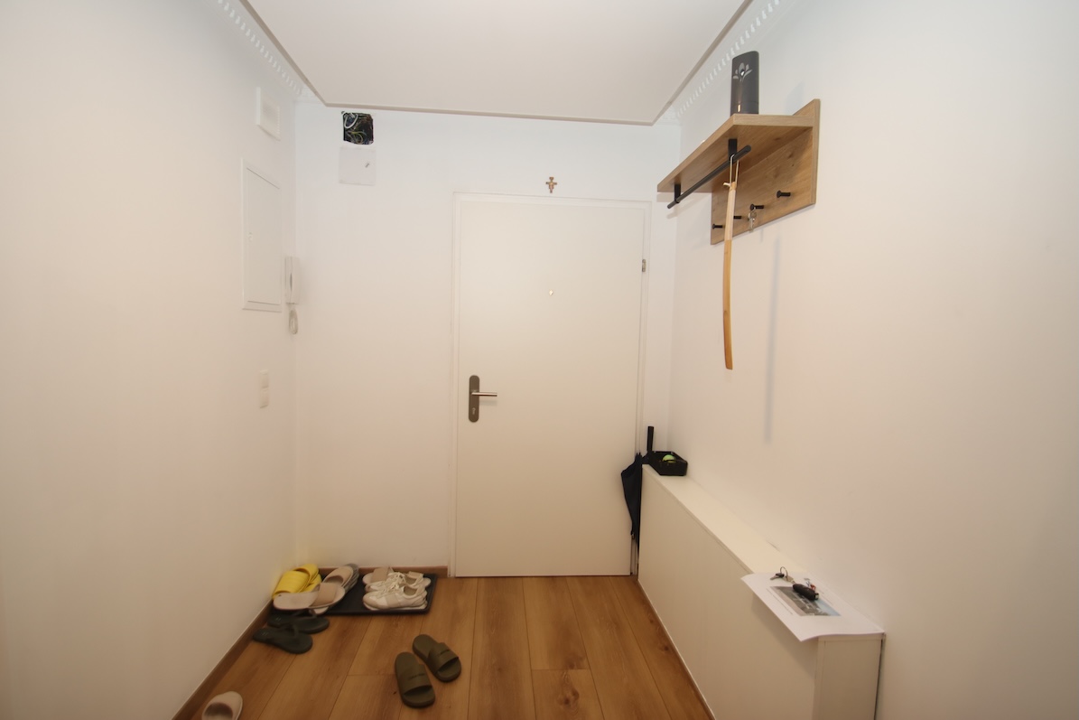 Vorraum mit weißer Tür, Garderobe und Schuhablage auf Parkettboden