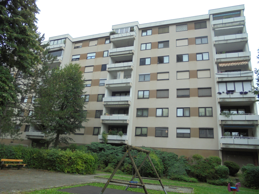Mehrfamilienhaus mit Balkonen und Bäumen im Vordergrund
