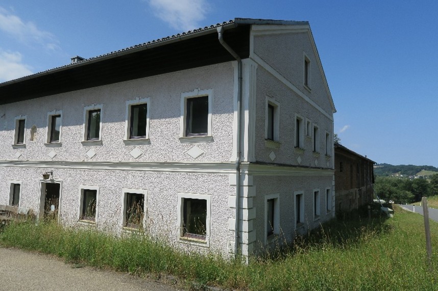 Landhaus in Österreich mit weißem Putz und dunklem Dach, umgeben von Grün.