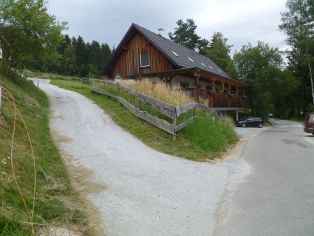 Holzhaus mit Veranda und Holzzaun an einer Weggabelung in ländlicher Umgebung