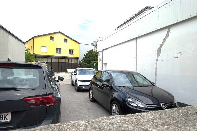 Autos parken vor gelbem Gebäude mit Rissen in der weißen Wand