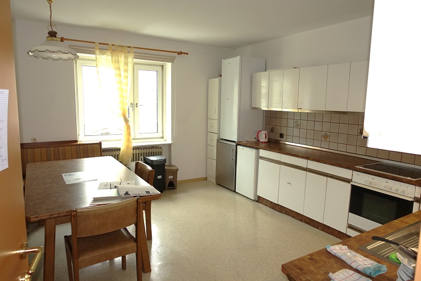 Küche mit Esstisch, Sitzbank und weißen Küchenmöbeln, Kühlschrank, Herd und Fenster