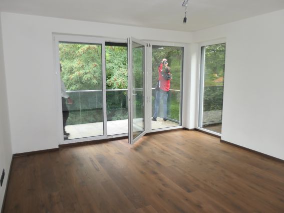 Frau mit roter Jacke fotografiert von Balkon in einem leeren Zimmer mit Parkett.