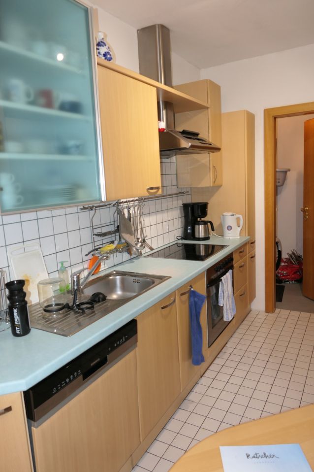 Küche mit Spüle, Kaffeemaschine, Herd und Tür zu einem weiteren Raum.