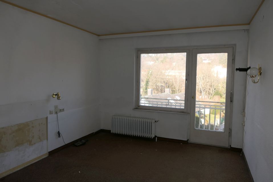 Innenansicht eines leeren Zimmers mit Fenster, Balkontür und Heizkörper