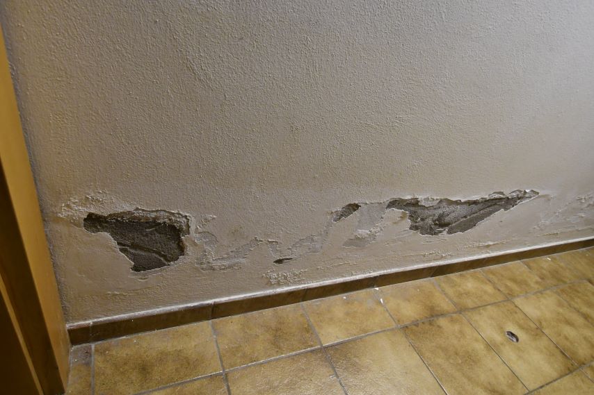 Wandputz löst sich ab und gibt Sicht auf Mauerwerk frei, Fliesenboden