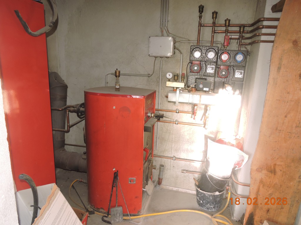 Heizkesselanlage mit rot lackiertem Kessel und Kupferrohrleitungen in einem Kellerraum.