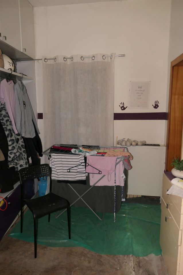 Wäscheständer mit Kleidung und schwarzer Stuhl auf grüner Unterlage in einem Raum
