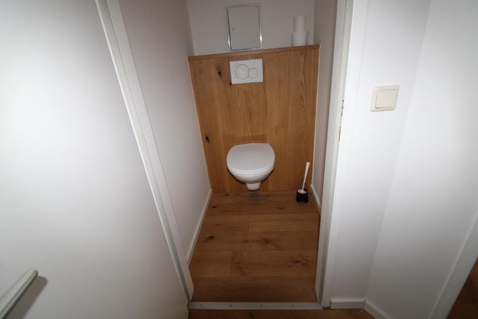 Toilet mit Holzwandverkleidung und Holzboden in einem schmalen Raum