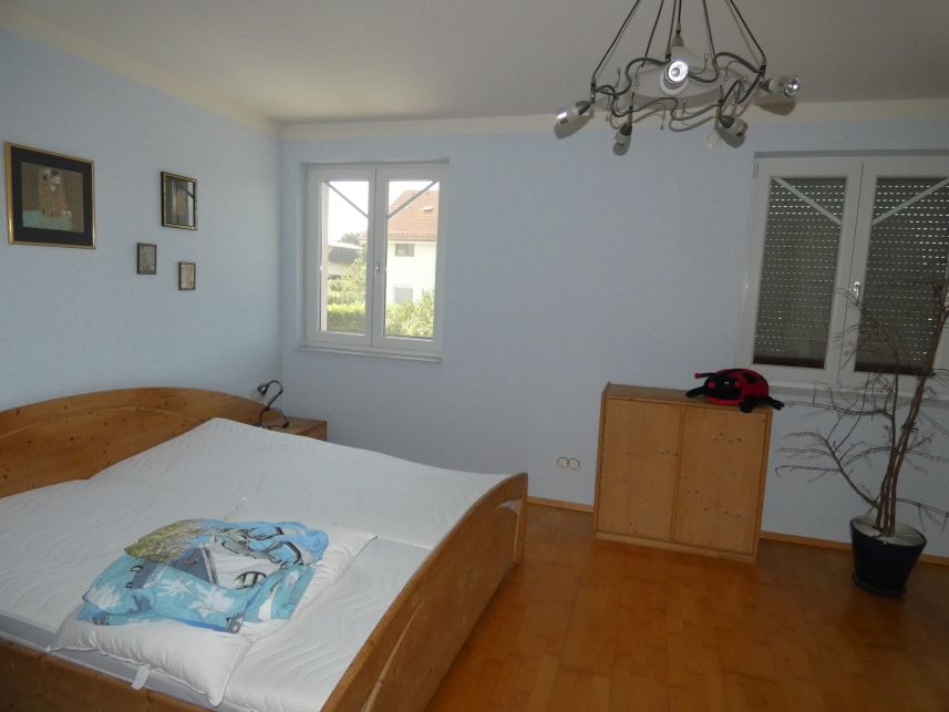 Schlafzimmer mit Holzbett, Nachtkästchen, Kommode und Fenster