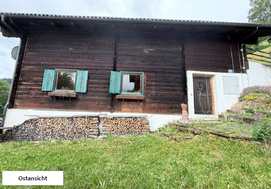 Holzhaus-Ostansicht mit zwei Fenstern, Holzlager und Eingangsbereich in den Bergen