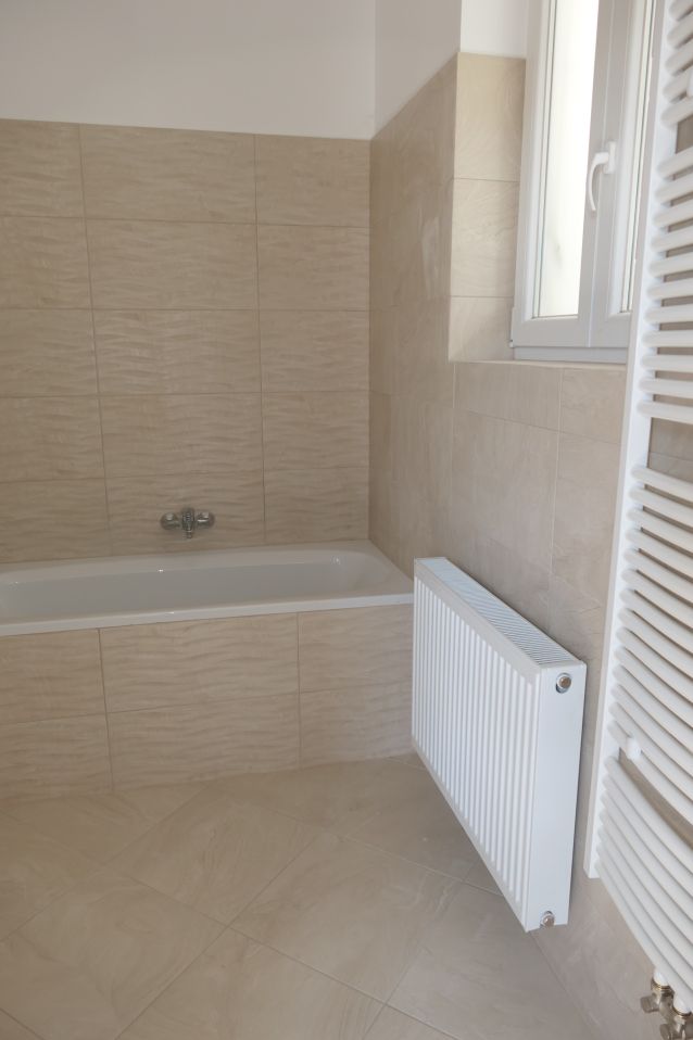 Badezimmer mit Badewanne, Heizkörper und Fenster, gefliest