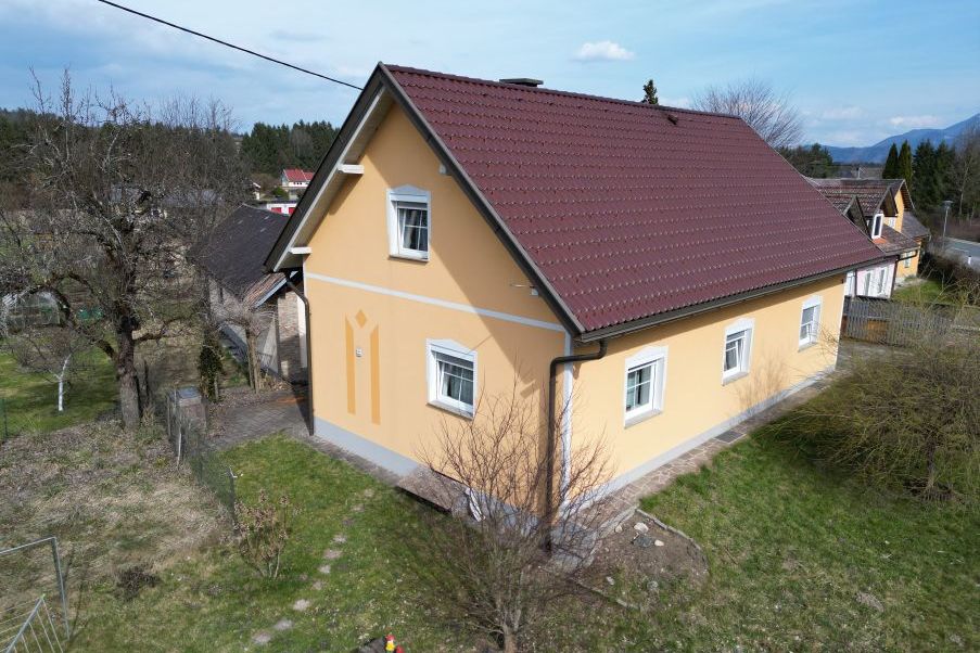 Gelbes Haus mit dunkelrotem Ziegeldach und Garten in ländlicher Umgebung