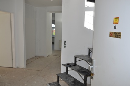 Treppenaufgang mit weißen Wänden und einer Tür mit Hinweisschildern in einem Haus