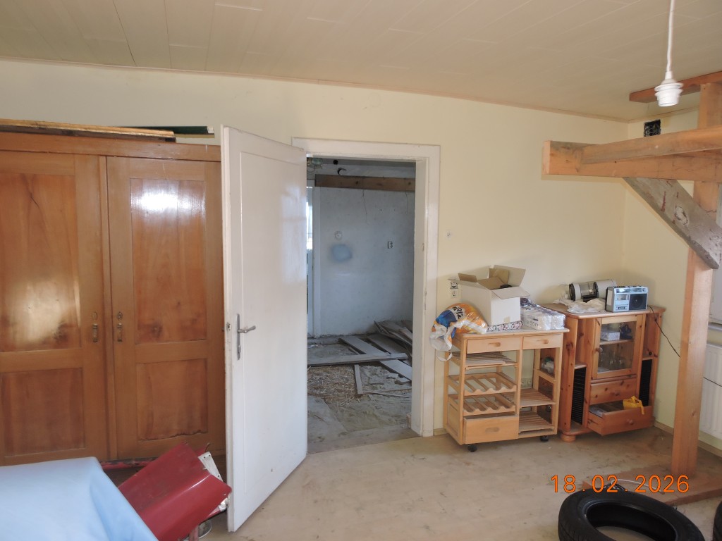 Holzschrank und offene Tür mit Blick in einen Rohbau, daneben Möbel