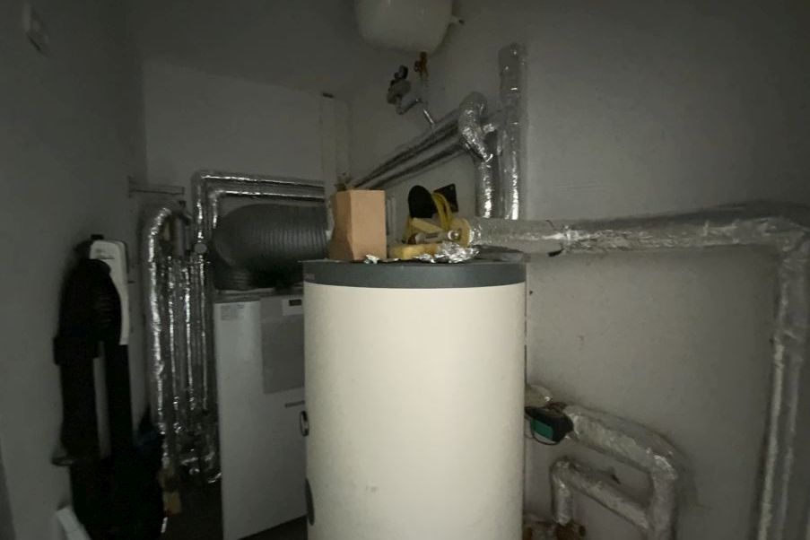 Heizungsanlage mit Warmwasserspeicher, Rohren und Lüftungsschacht in einem Technikraum