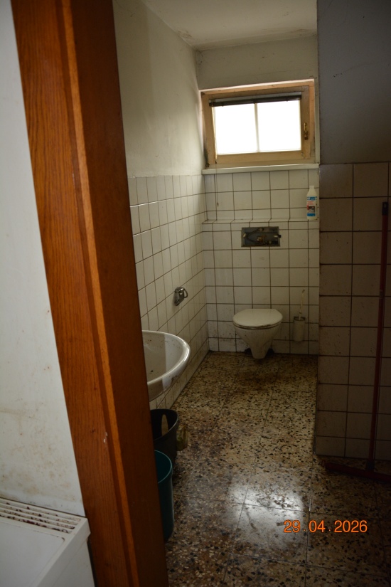 Toilette und Waschbecken mit Fliesenwand und Fenster in einem schmutzigen Badezimmer