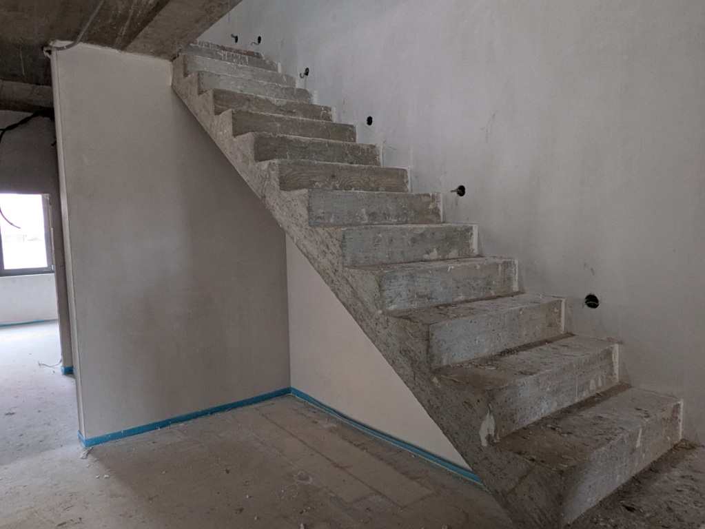 Betontreppe im Rohbau mit unfertigen Wänden und Boden in einem Gebäude.