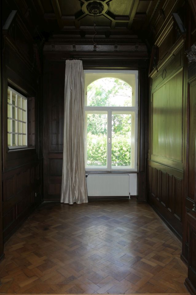 Parkettboden und Holztäfelung in einem Raum mit großem Bogenfenster und Heizkörper
