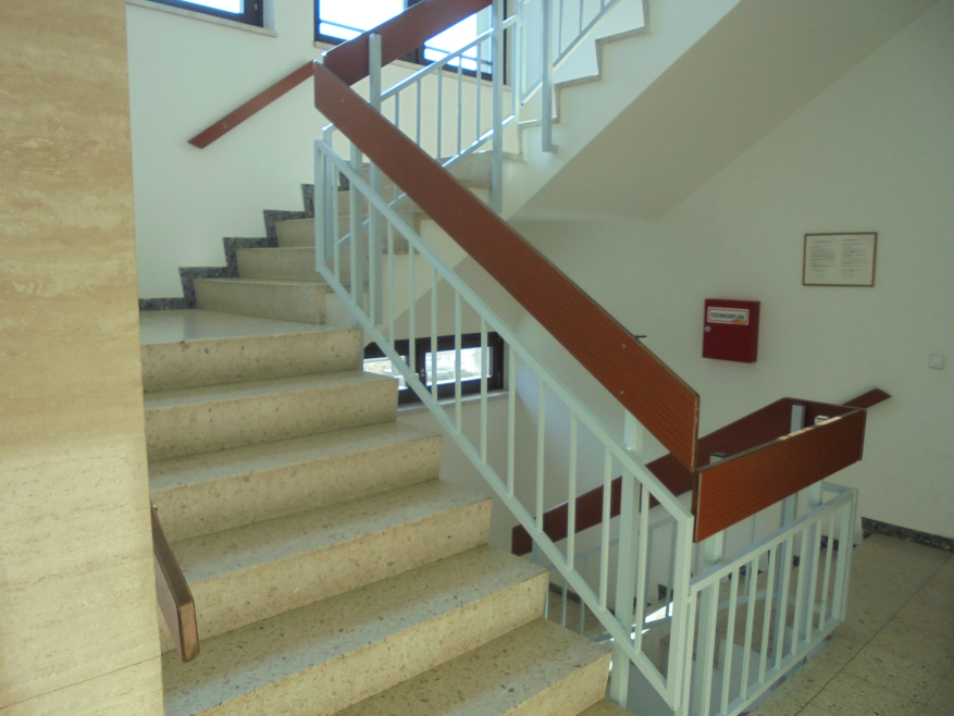 Betontreppe mit Holzhandlauf und weißem Geländer im Inneren eines Gebäudes