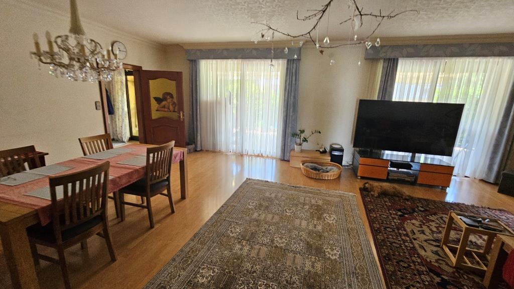 Esszimmer mit Holztisch, vier Stühlen und einem Hund vor dem Fernseher