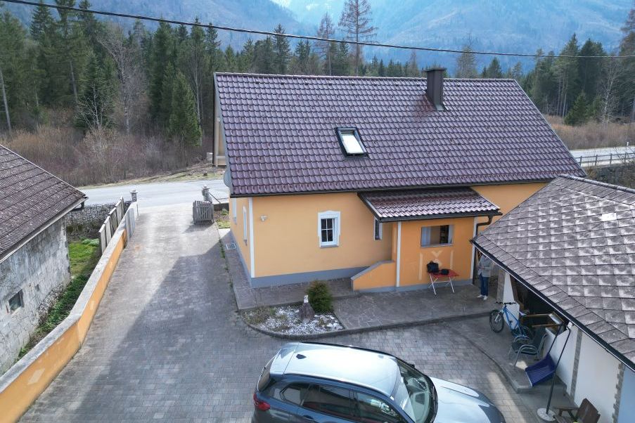 Gelbes Haus in Bergkulisse mit Autos und Fahrrädern vor dem Eingang