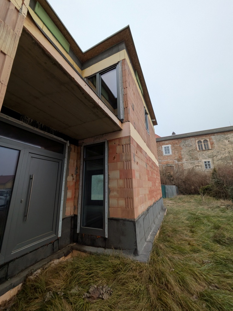 Neubau Ziegelhaus mit Fenster und Tür im Vordergrund, altes Gebäude im Hintergrund