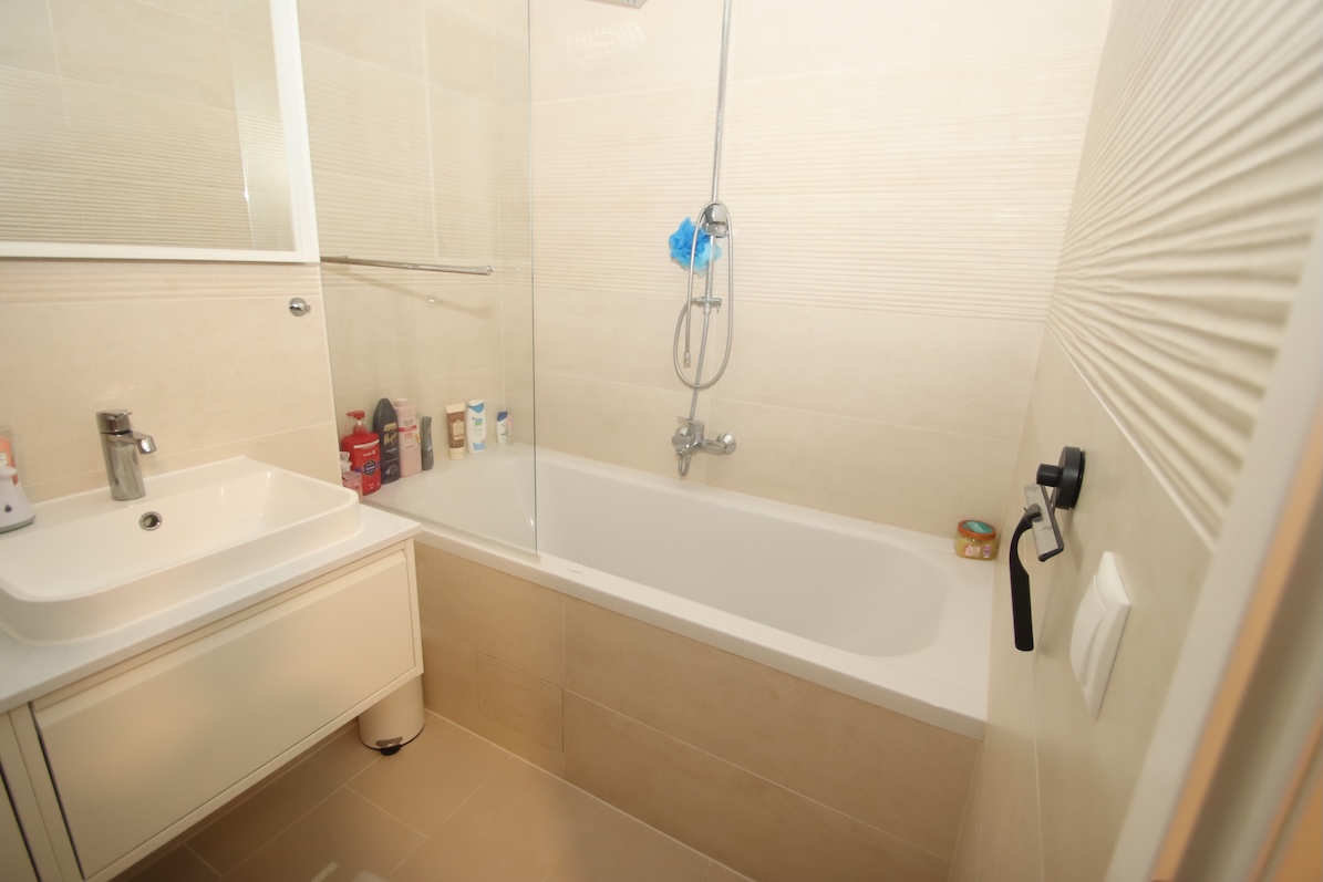 Badezimmer mit Waschbecken, Badewanne und Duscharmatur, hell gefliest