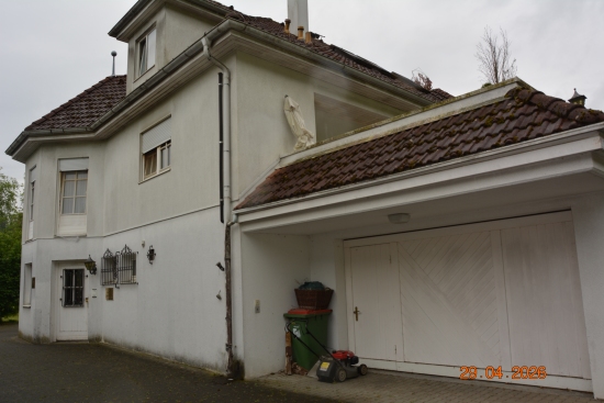 Haus mit Garage, Rasenmäher und Mülltonne vor weißem Tor, 28.04.2023