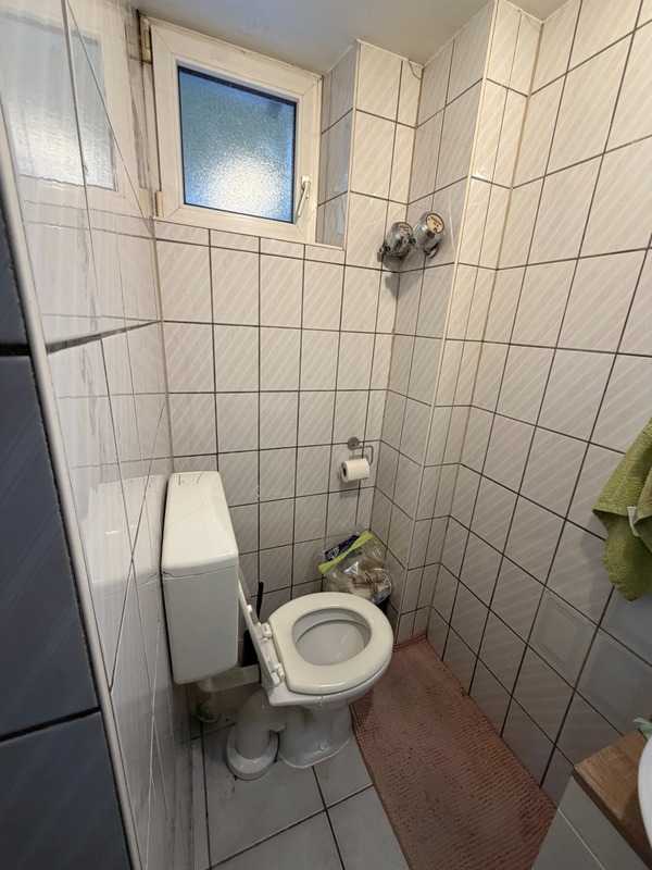 Toilette mit Spülkasten in einem gefliesten Badezimmer mit kleinem Fenster