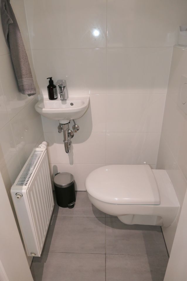 Toilette mit kleinem Waschbecken, Mülleimer und Heizkörper in einem Badezimmer