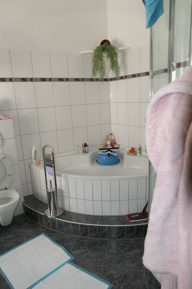 Badezimmer mit Eckbadewanne, Toilette, Duschkopf und rosa Bademantel