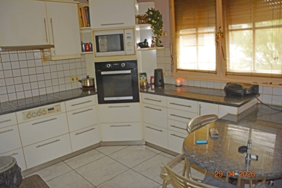 Küche mit weißen Einbauschränken, Mikrowelle, Backofen und Rundtisch