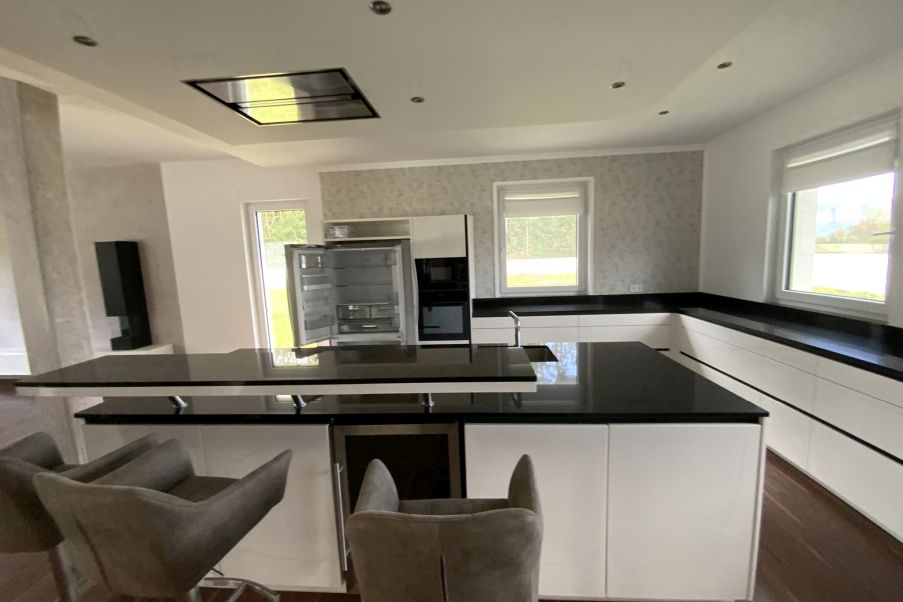 Moderne Küche mit schwarzer Arbeitsplatte, Kühlschrank und Barhockern