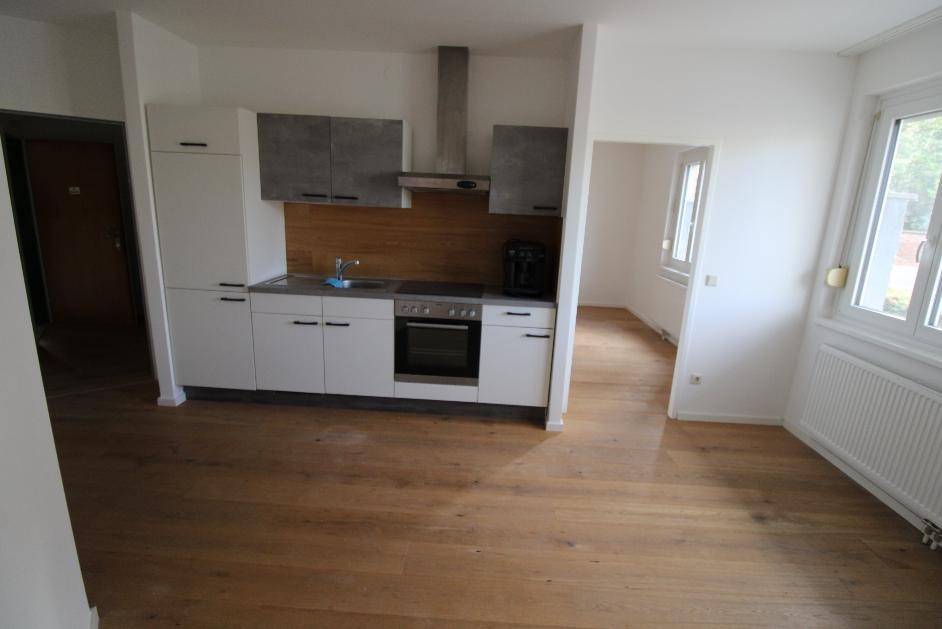 Küche mit weißen Unterschränken und grauen Hängeschränken, Holzboden und Durchgang zu einem weiteren Raum.